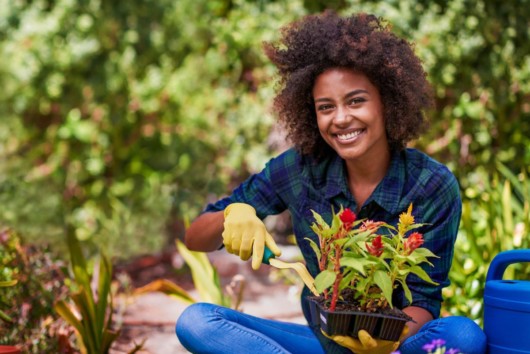 A girl is holding a flower in the pot. She is doing gardening to reduce stress