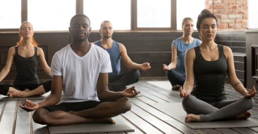 Group of people are sitting on the floor with closed eyes and doing yoga