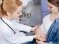 Professional obstetrician providing proficient checkup while examining pregnant belly