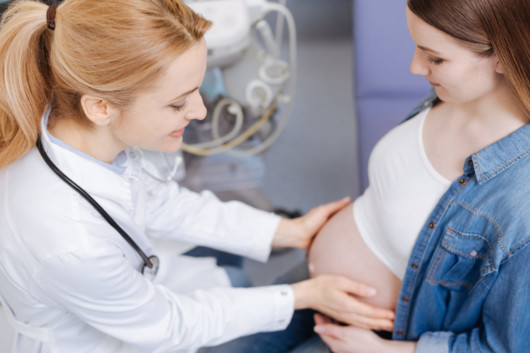 Professional obstetrician providing proficient checkup while examining pregnant belly