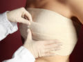 A doctor is putting a post surgical bandages on the girl's breast after the breast augmentation procedure