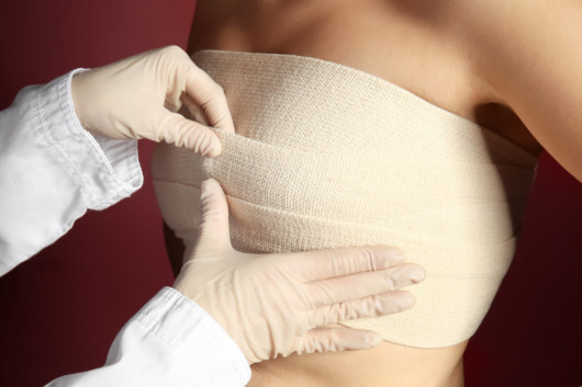 A doctor is putting a post surgical bandages on the girl's breast after the breast augmentation procedure