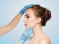 A close up face of a woman on blue background with the doctor's hands on it.