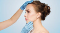 A close up face of a woman on blue background with the doctor's hands on it.