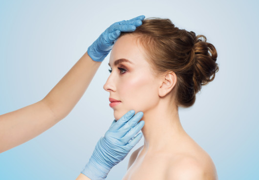 A close up face of a woman on blue background with the doctor's hands on it.