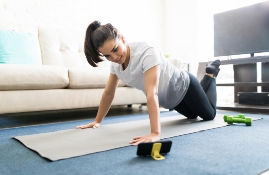 Girl is using fitness application on her sell phone to workout at home to stay fit