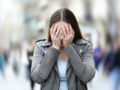 The girl is covering her face with her hands because she is suffering panic attack on city street