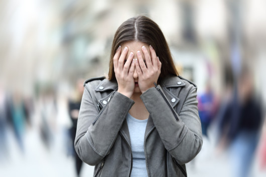 The girl is covering her face with her hands because she is suffering panic attack on city street