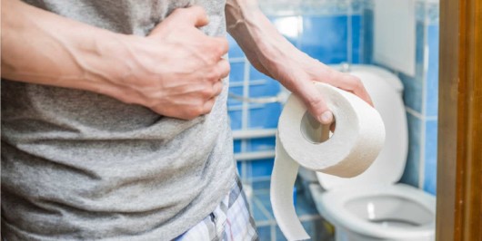 A gut with a roll of toilet paper in his hand in the toilet. he is holding his stomach with one hand