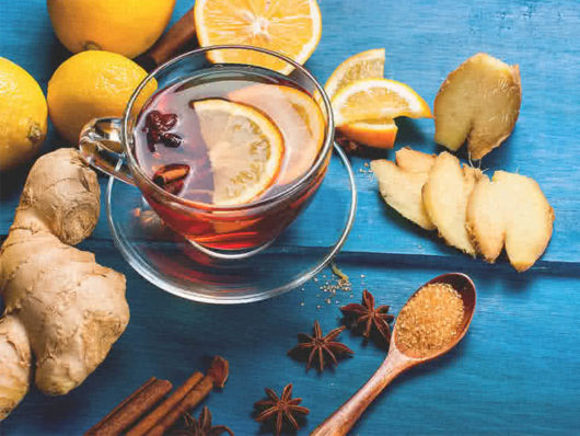 Tea in a transparent cup with ginger and orange around on the blue background