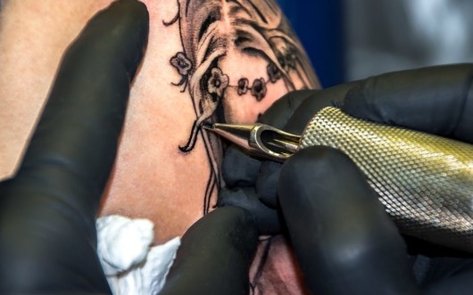 A close up picture of tattoo maker who is doing tattoo on shoulder