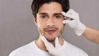 A close up face of the guy on grey with doctor's hands on his face.