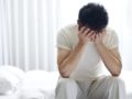 A young guys sits on the bed and covers his face with hands