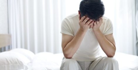 A young guys sits on the bed and covers his face with hands
