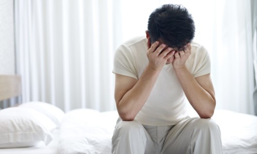 A young guys sits on the bed and covers his face with hands