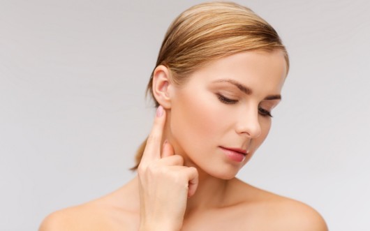 A blonde girl on white background who points at the ear