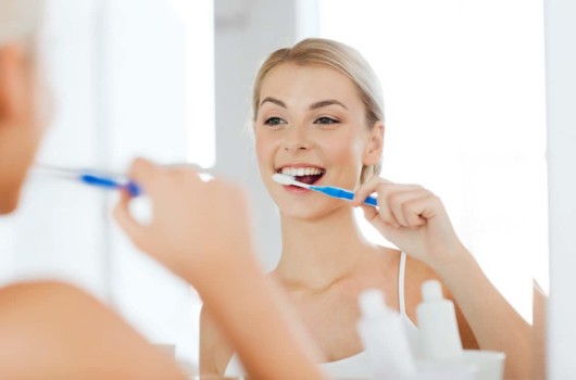 A blonde girl is cleaning her teeth with a tooth brush in a bathroom