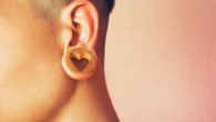 A close up picture of the ear with a tunnel and a wooden earring in the shape of heart