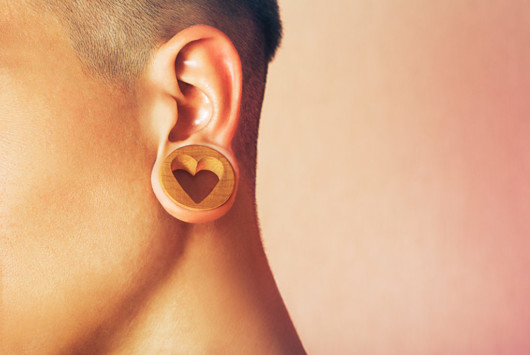 A close up picture of the ear with a tunnel and a wooden earring in the shape of heart