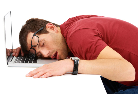 A guy is sleeping on his working table in front of the computer