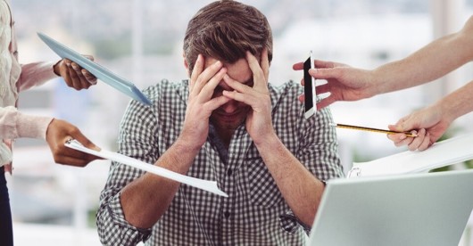 a stressed guy is sitting at the table at work and covers his face with hands