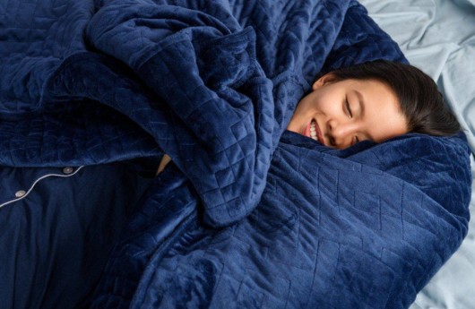 A young girl wrapped herself in a blue weighted blanket on the bed