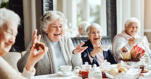Senior ladies are sitting at the table, smiling, talking and having tea