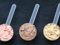 Three portions of pre-workout powders of different colors on grey background