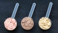 Three portions of pre-workout powders of different colors on grey background