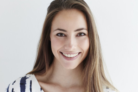 A close up portrait of a young woman with even and nice teeth after Invisalign braces.