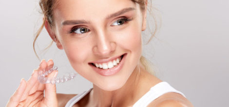 A close up picture of a young smiling girl who is holding Invisalign brace in her hand