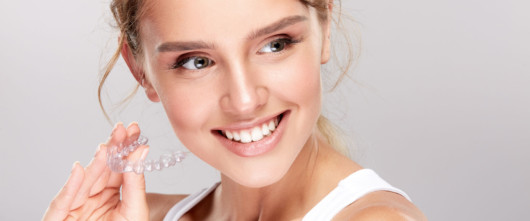 A close up picture of a young smiling girl who is holding Invisalign brace in her hand