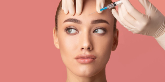 A close up face of a girl on pinky background with a botox shot at her forehead