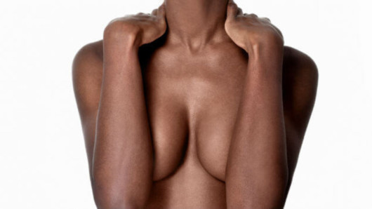 A torso of a black woman who covers her breasts with arms