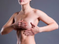 A close up body of woman on grey background who is holding her breast