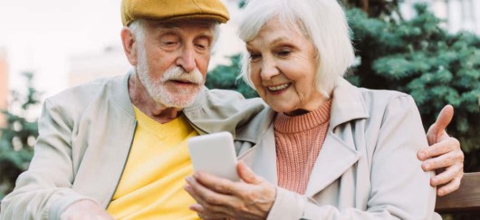 A senior man and a woman are sitting together and looking into the telephone