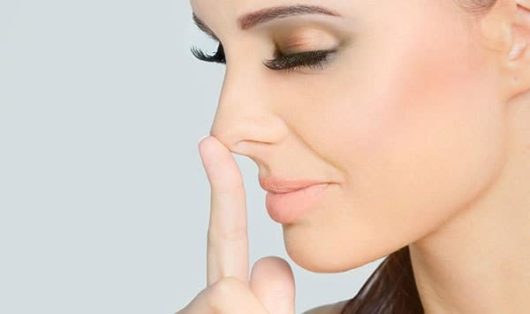 A beautiful woman with closed eyes is touching her nose with a finger