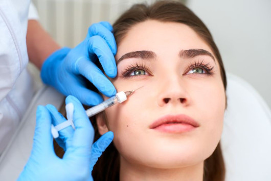 A doctor in blue gloves is doing botox shot to the girl