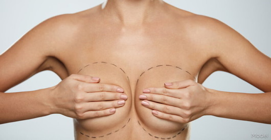 A close up picture of a woman breasts covered by woman's hands on white