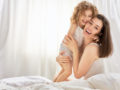 A happy mom and a child is embracing and laughing on the bed
