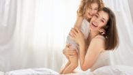 A happy mom and a child is embracing and laughing on the bed