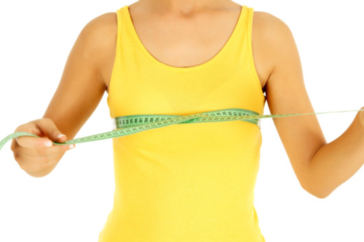 A torso of a woman with small breasts in yellow undershirt on white background