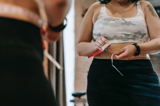 A woman measuring her waist with a tape measure.