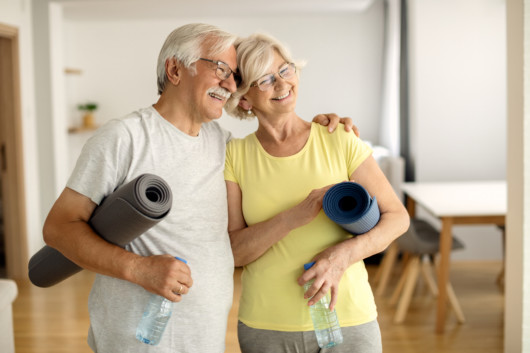 Happy senior husband and wife feeling satisfied after exercising and embracing at home.