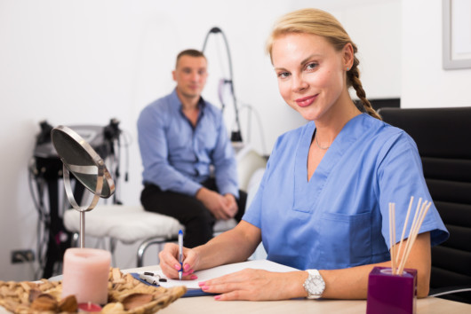 Woman specialist is writing the conclusion after procedure for man in clinic.